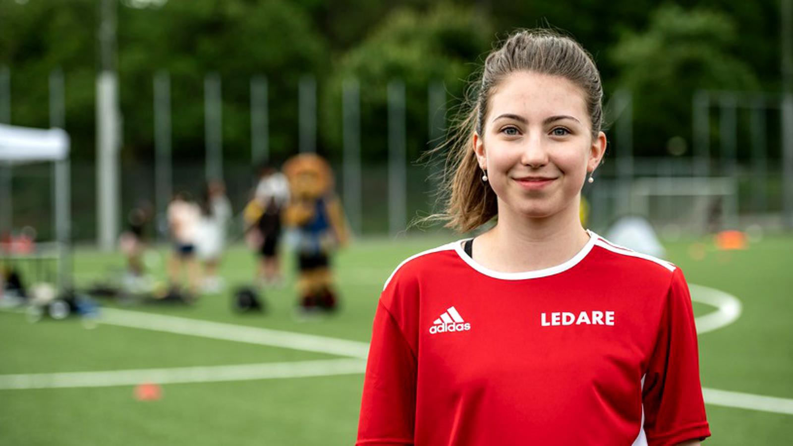 En bild på Julia Kaslin som är ny som ledare. Hon står på en fotbollsplan och bär en tröja med texten "Ledare" på.