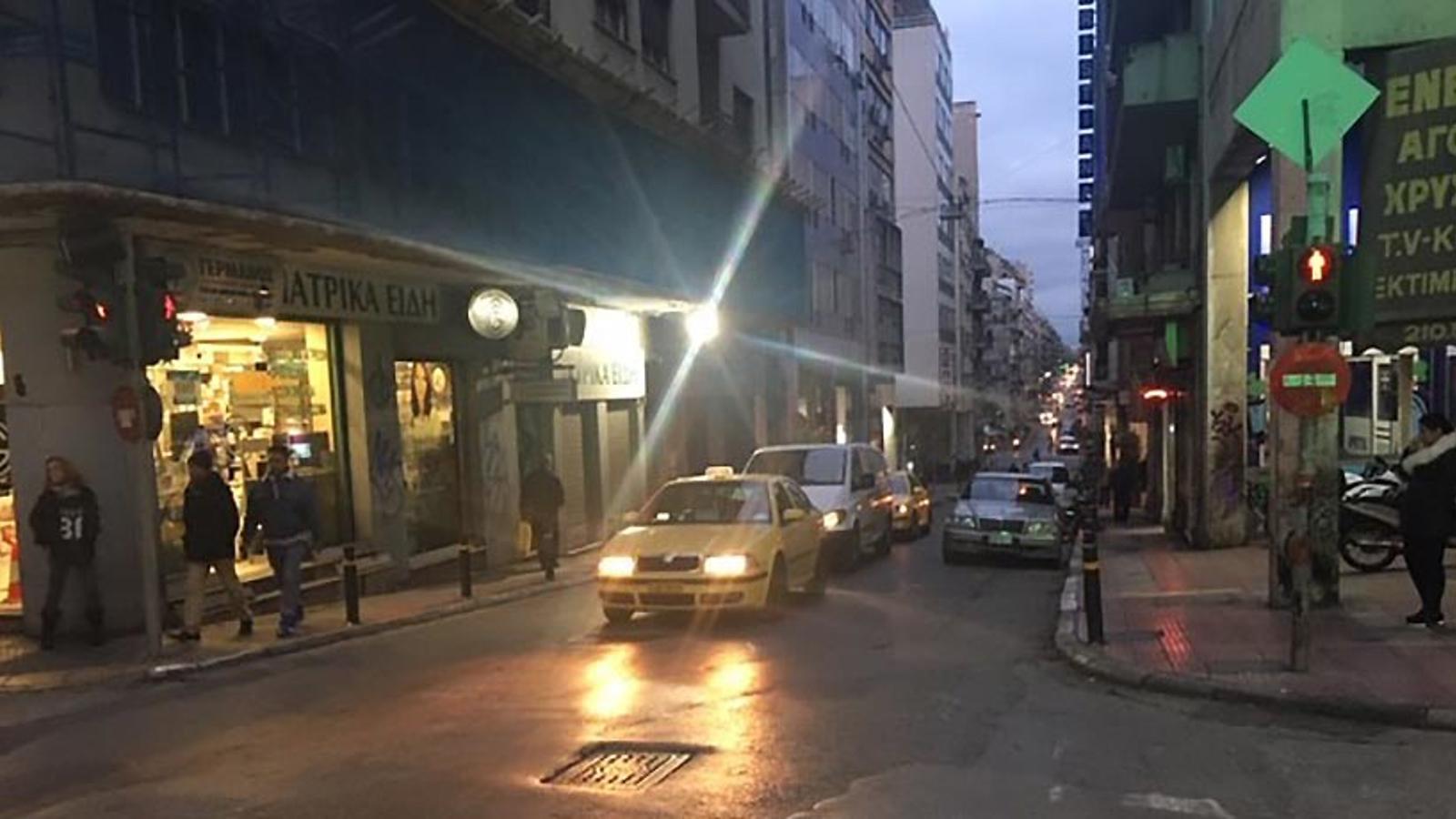 Det tuffa kvarteret Omonia i Aten, där bilar kommer åkandes på en bilväg. Till vänster och höger om bilvägen går det människor på gatorna.