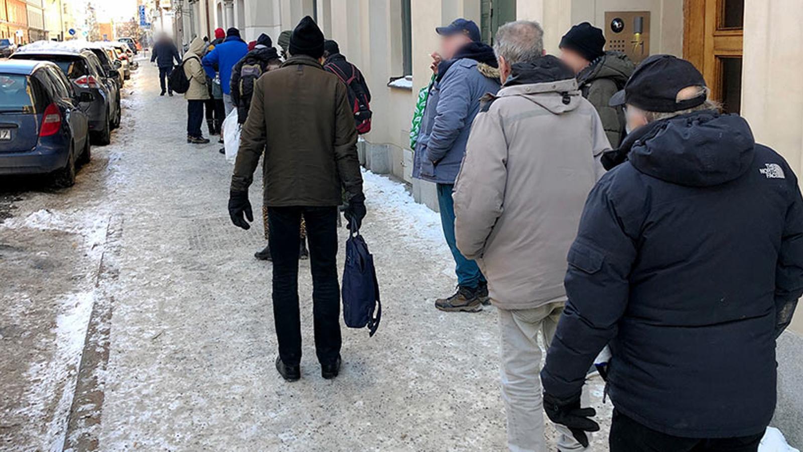 En lång kö av hjälpsökande som står längs med en gata utanför Templet i Stockholm. Personerna i kön står med ryggtavlorna mot kameran.
