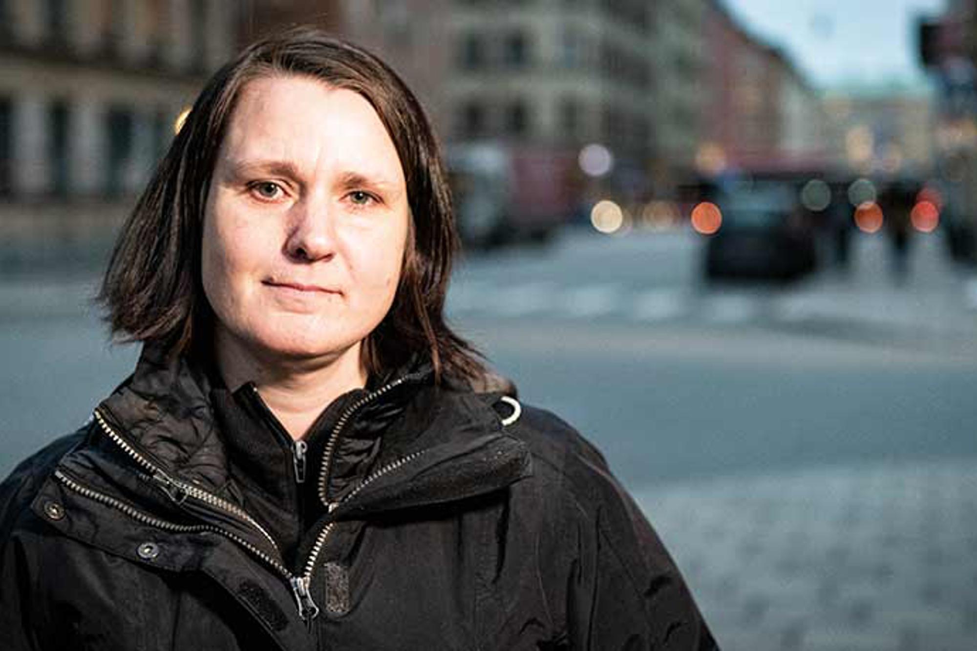 Porträttbild av Kamilla Lindstedt som tittar in i kameran. Hon står utomhus på en gatan, och i bakgrunden syns byggnader.