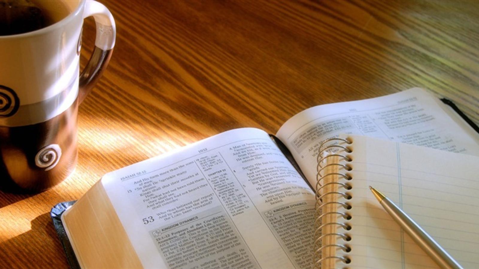 En uppslagen bibel som ligger på ett bord. På bibeln ligger det ett anteckningsblock och en penna.