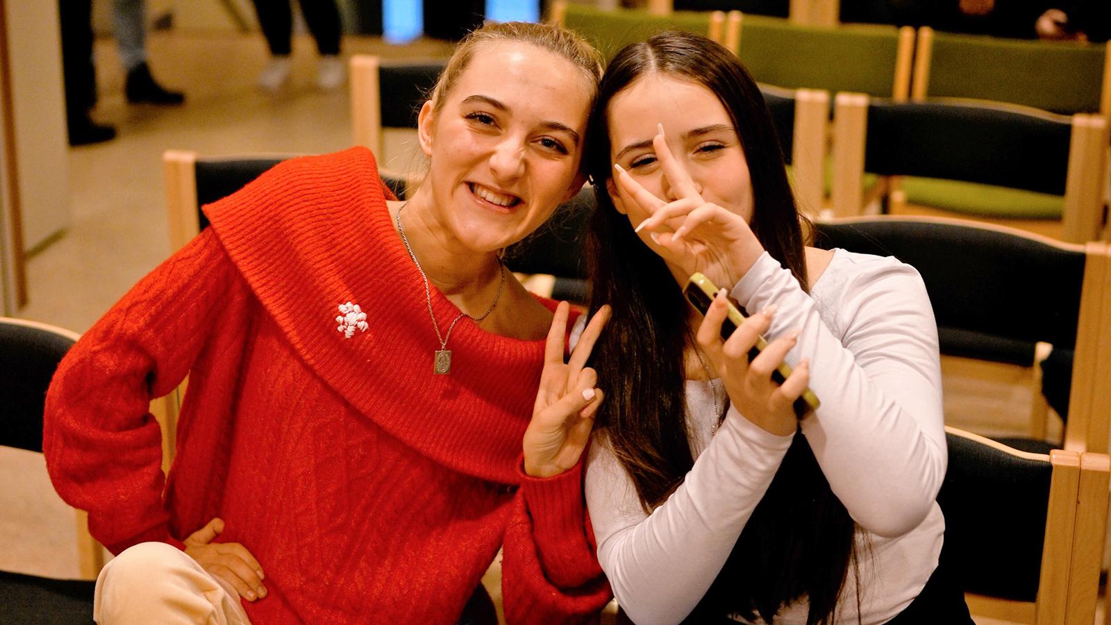 Två tjejer som kollar in i kameran och gör peace-tecknet med sina fingrar.