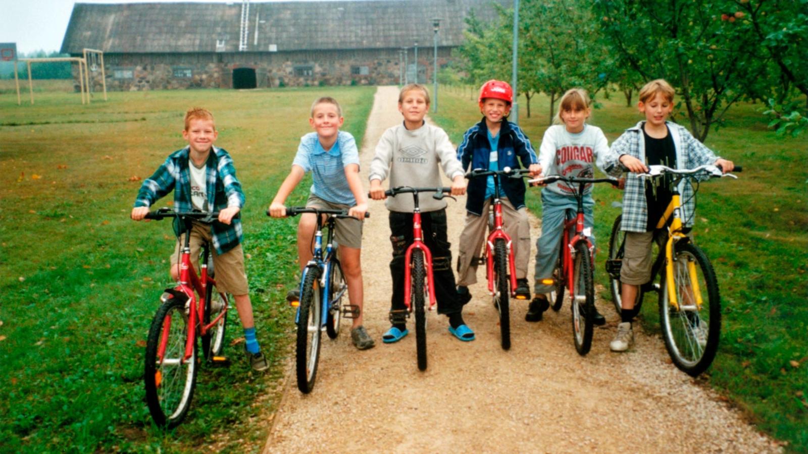 6 barn i 10-årsåldern står uppradade med varsin cykel på en grusväg.
