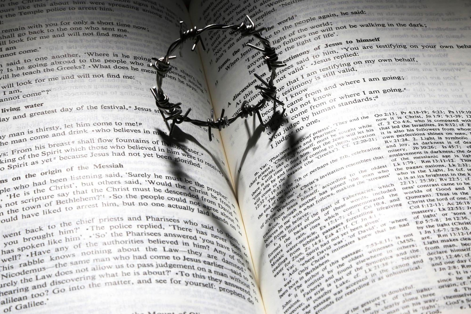 En uppslagen bibel med en ring som ser ut som ser ut som en törnekrona i uppslaget och skuggan av ringen blir ett hjärta.