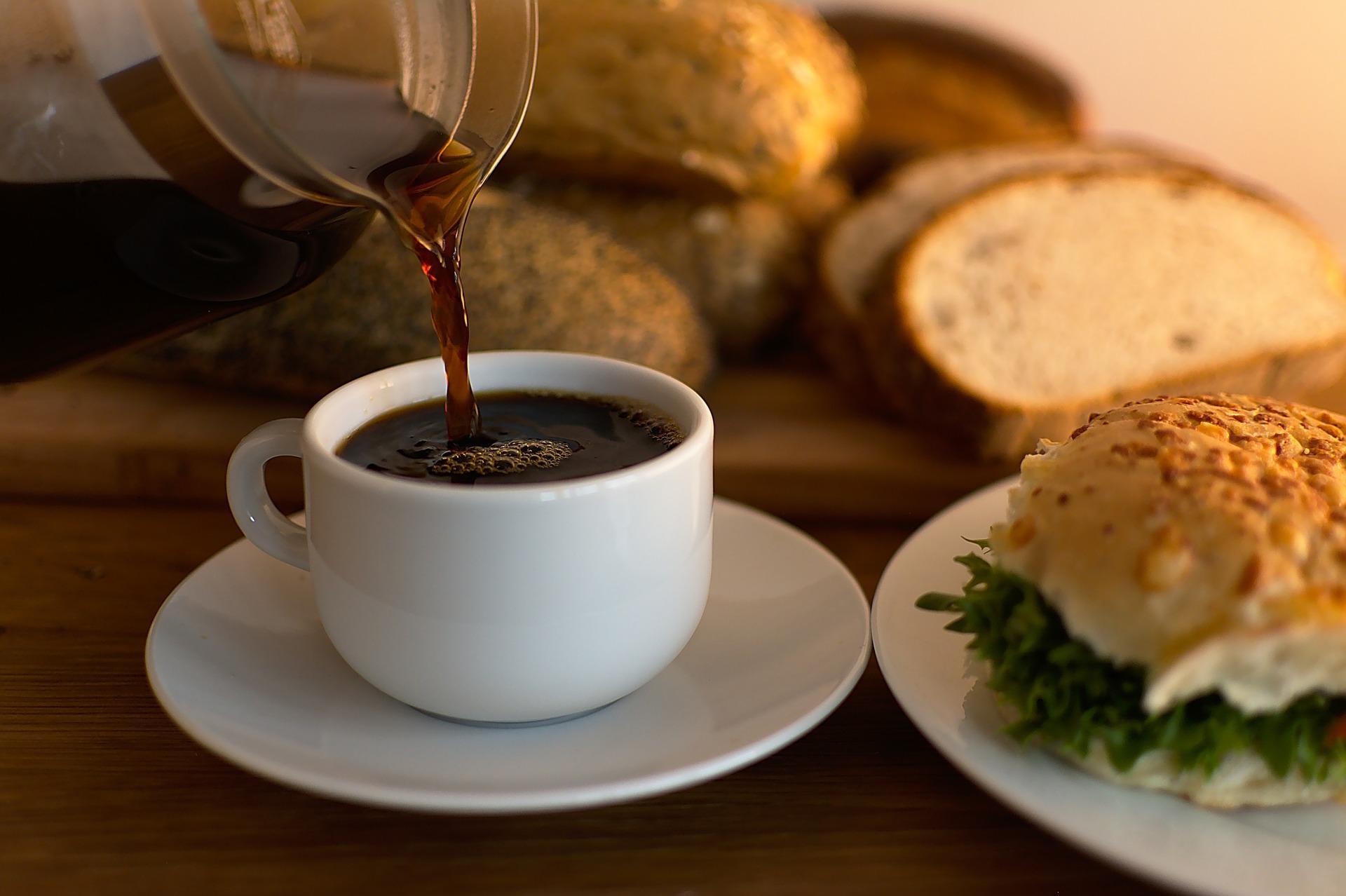 Kaffe hälls i en kopp med bröd i bakgrunden