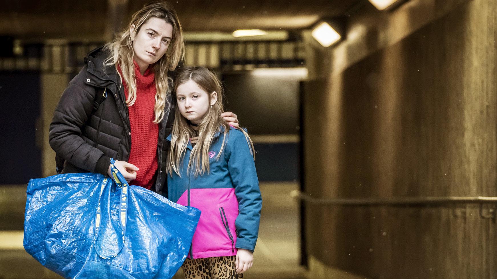 En ung mamma med en liten flicka står ensamma i ett parkeringsgarage - mamman håller i en ikea-kasse.