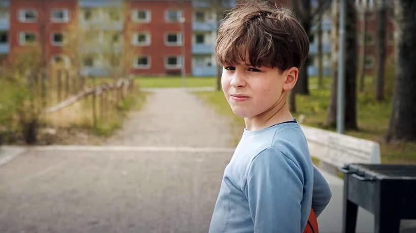 En ung pojke som står utomhus och tittar ledsamt förbi kameran.
