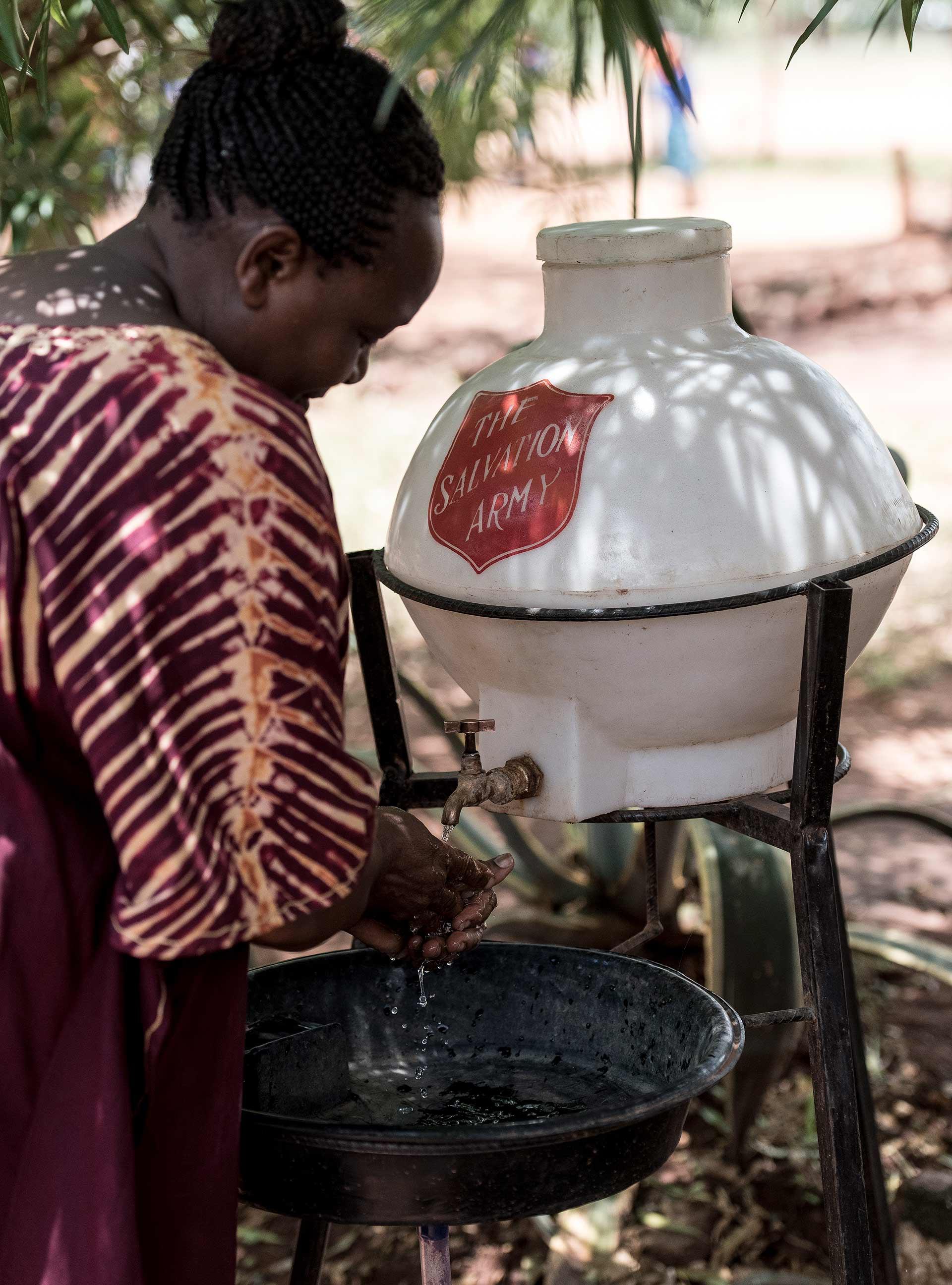 En afrikansk kvinna tvättar händerna vid en vattenbehållare som har Frälsningsarméns sköld.
