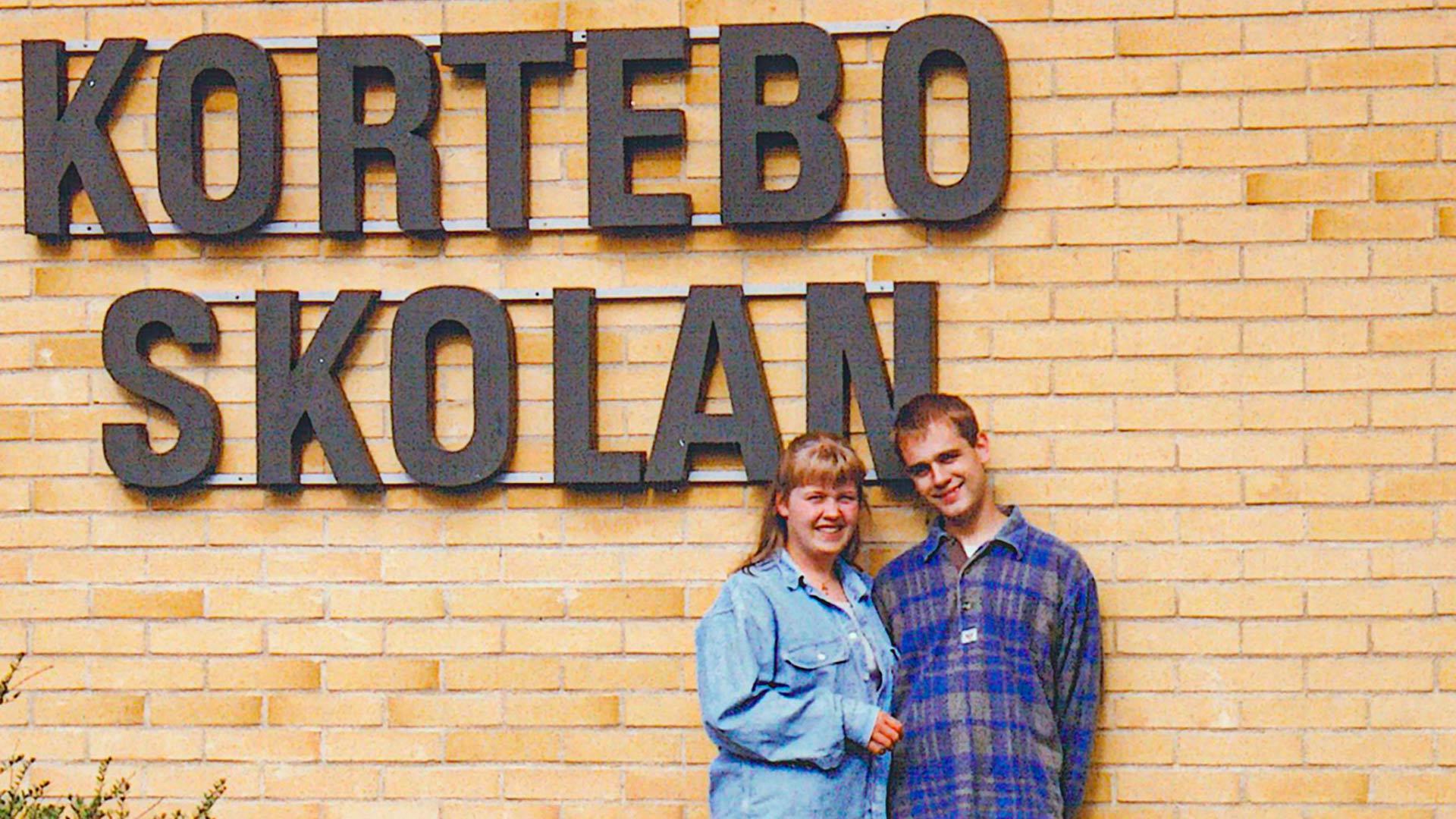 Elisabeth och Johan Grahn står framför en tegelvägg. En skylt sitter på väggen ovanför dem som det står Korteboskolan på