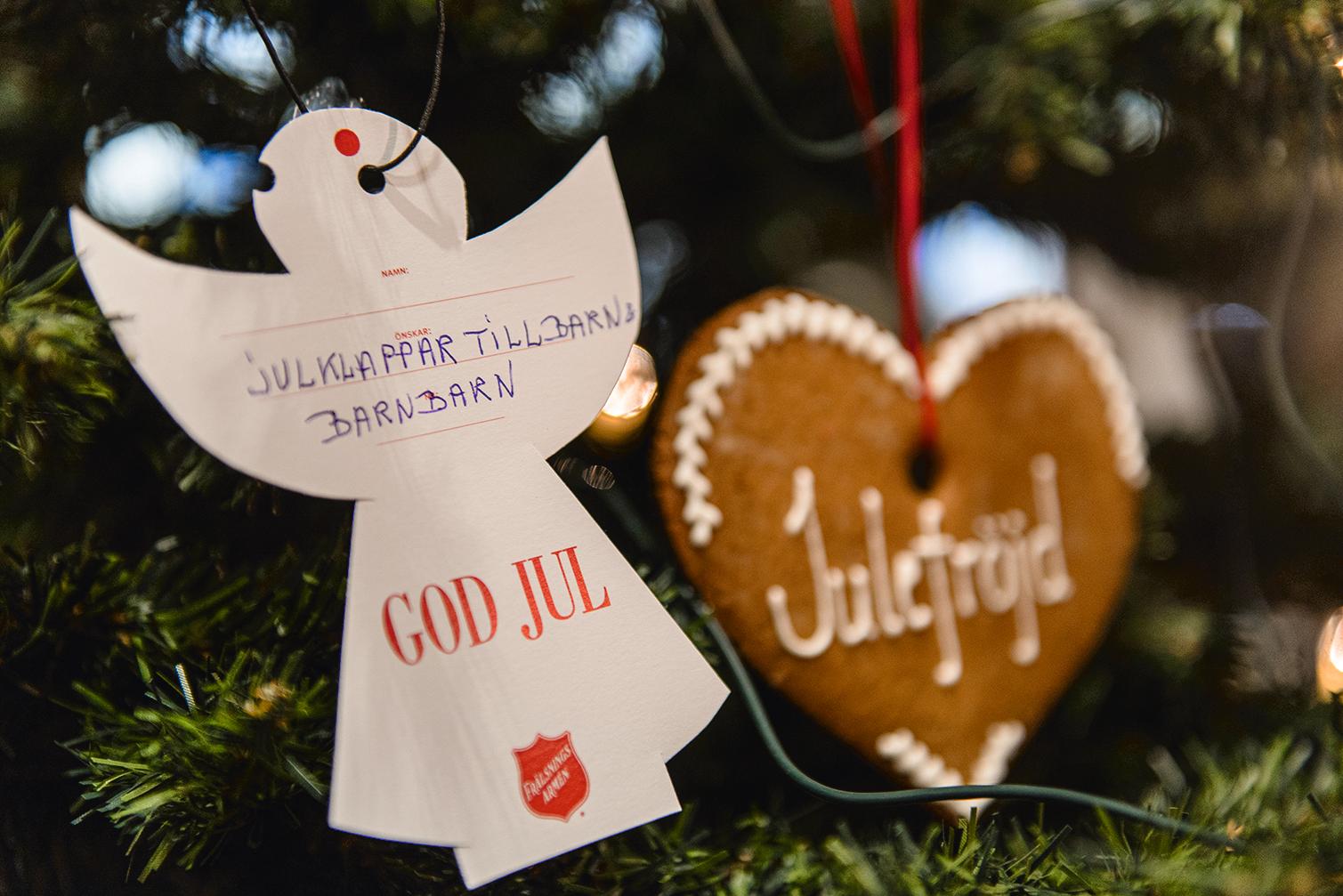 På en julgran hänger en pappershängel med en önskan om en julklapp till ett barn.