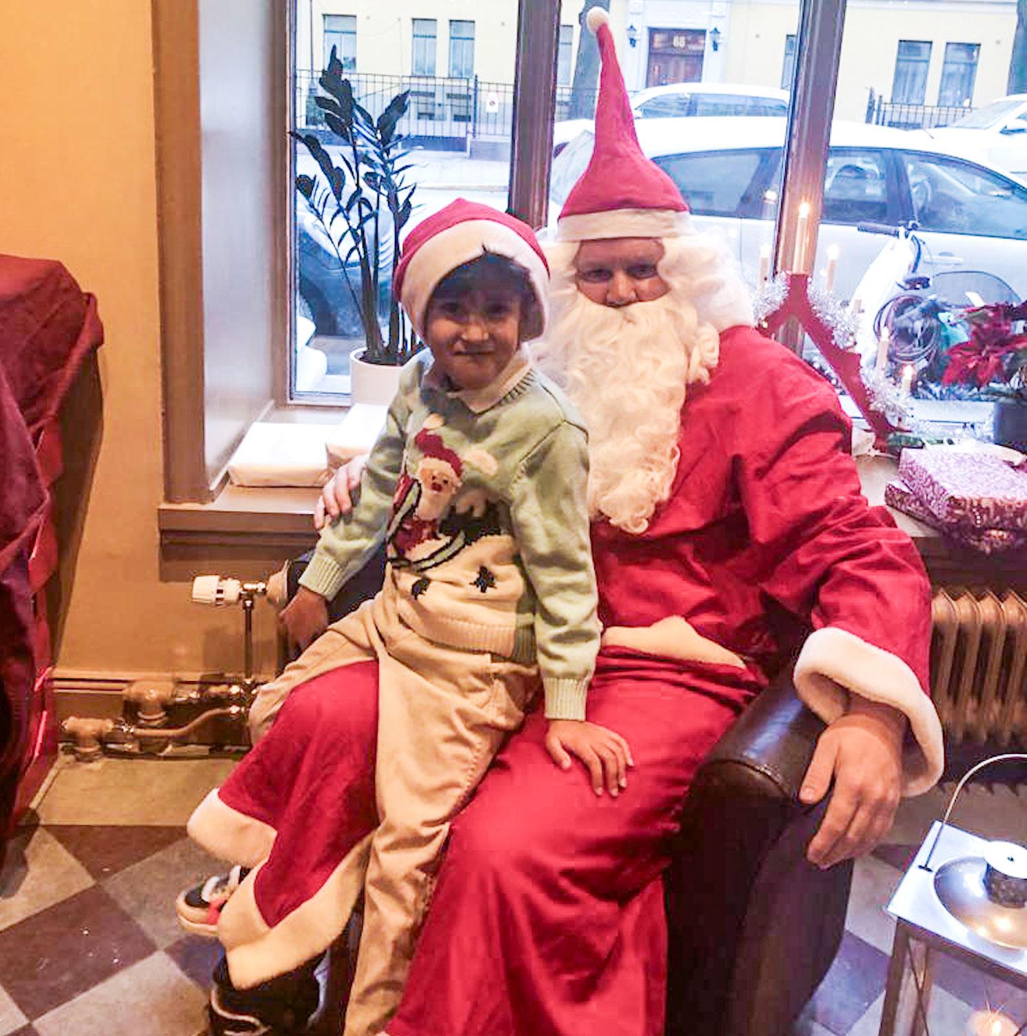 En glad liten pojke sitter i knät på någon som är utklädd till tomte.