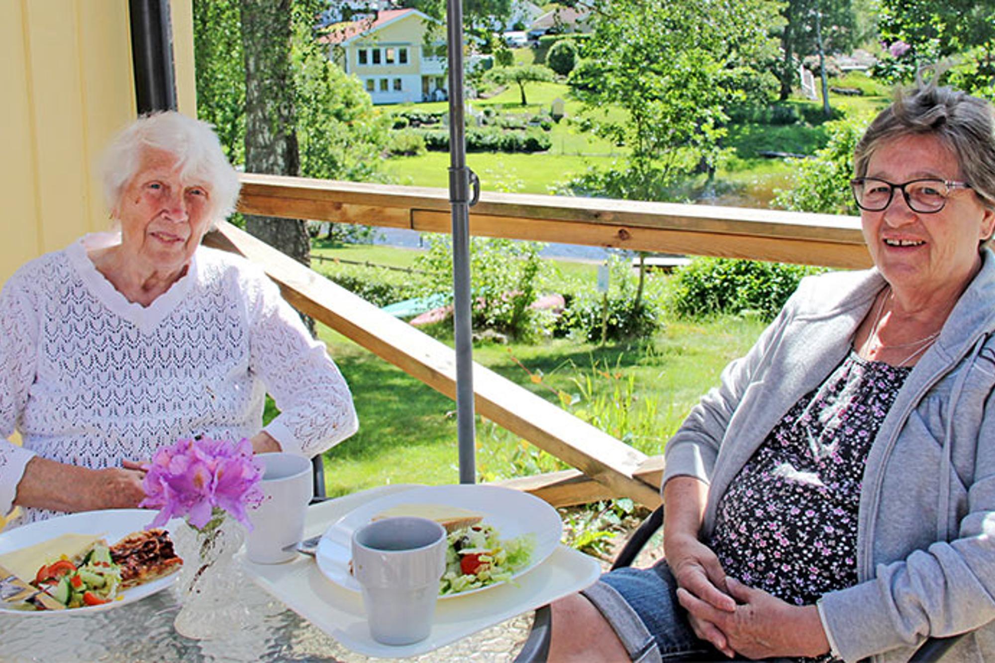 Två äldre damer som äter lunch på natursköna Kafé Salome i Alingsås. De sitter utomhus vid ett bord, under ett parasoll, och tittar in i kameran.