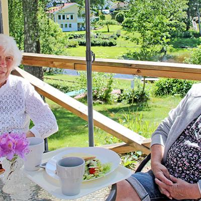 Två äldre damer som äter lunch på natursköna Kafé Salome i Alingsås. De sitter utomhus vid ett bord, under ett parasoll, och tittar in i kameran.