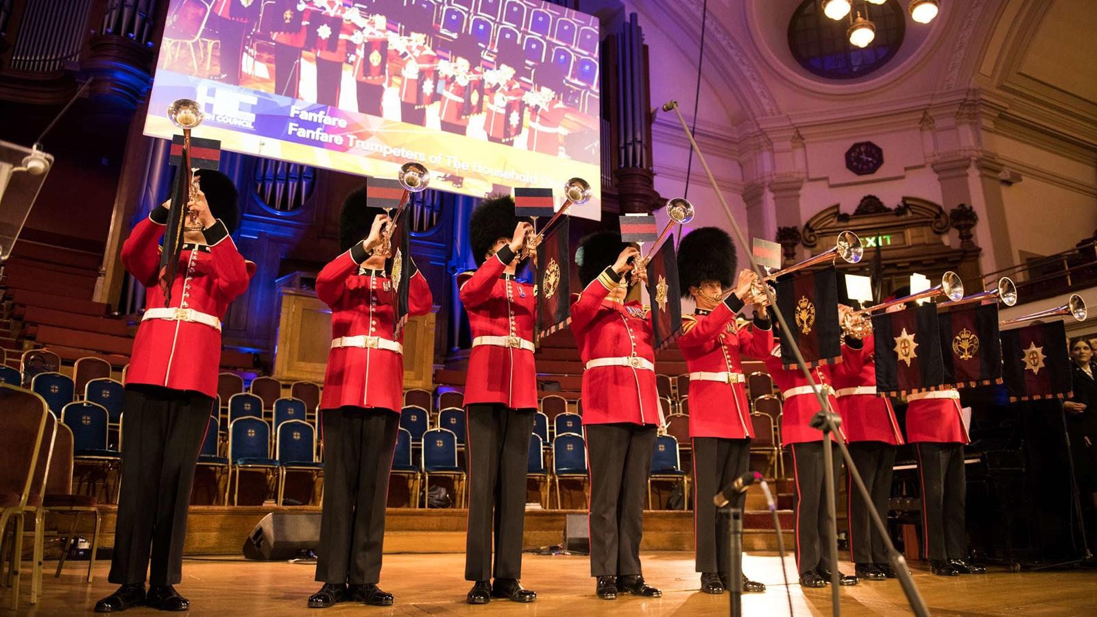 Åtta stycken musikanter i röd uniform står på scenen och blåser fanfar vid valet av Frälsningsarméns general 2018.
