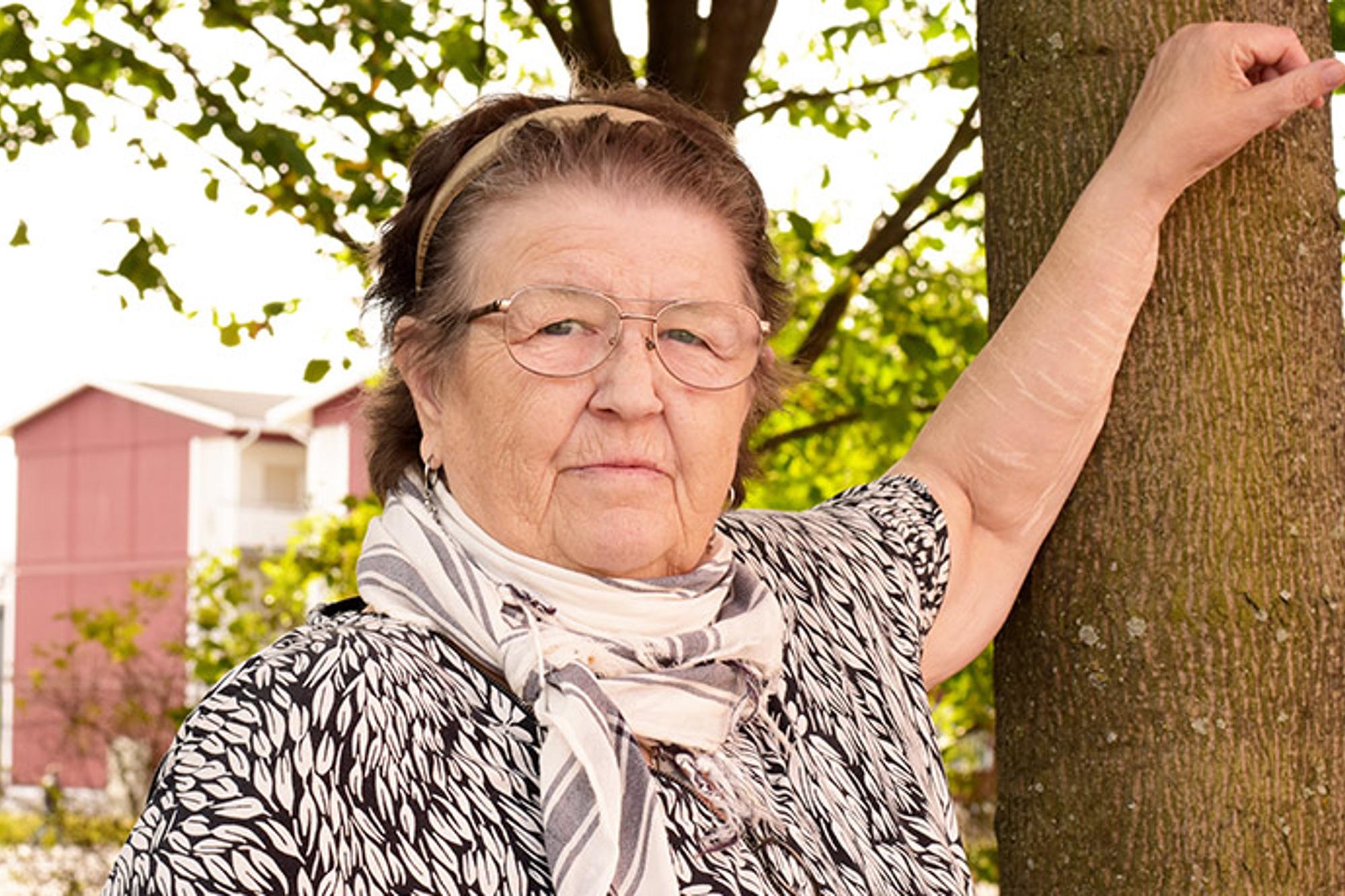 Porträttbild av Agneta Landfors som har ena armen mot ett träd. Hon tittar in i kameran.