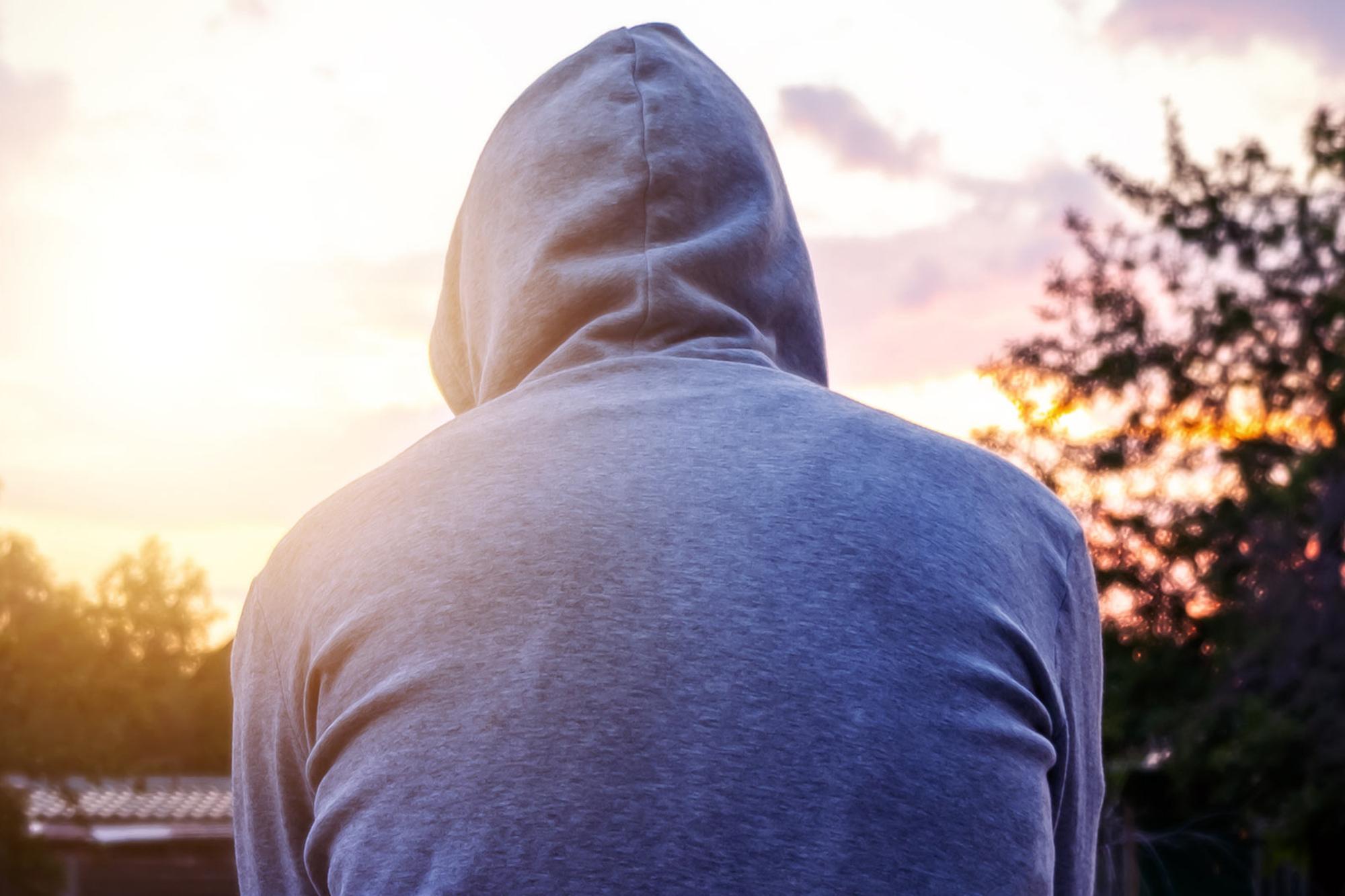 En ryggtavla på en person i hoodie i förgrunden med en solnedgång i bakgrunden.