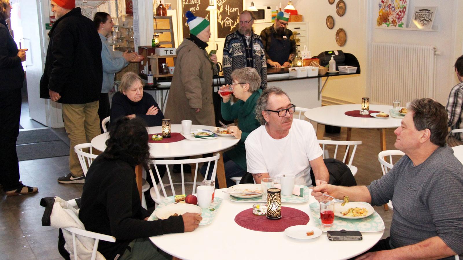 Människor sitter och äter och fikar runt borden på kaféet hos Frälsningsarmén i Östersund.