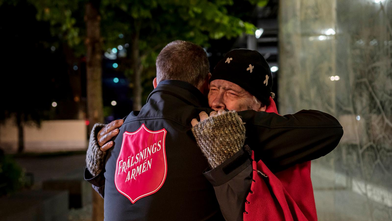 En hemlös man får en kram av en person med Frälsningsarméns sköld på ryggen