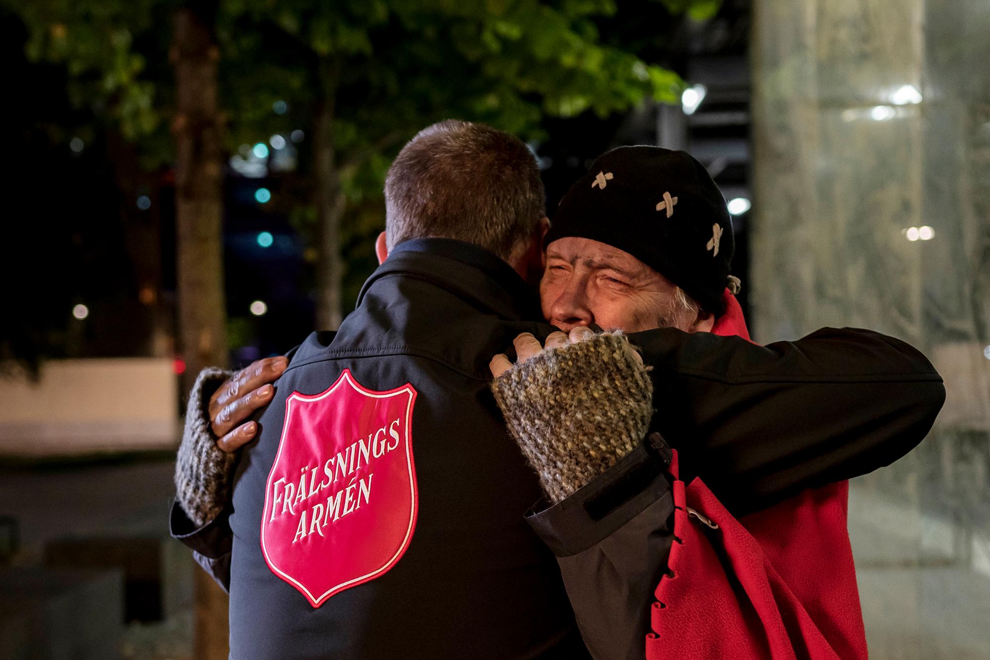 En hemlös man får en kram av en person med Frälsningsarméns sköld på ryggen