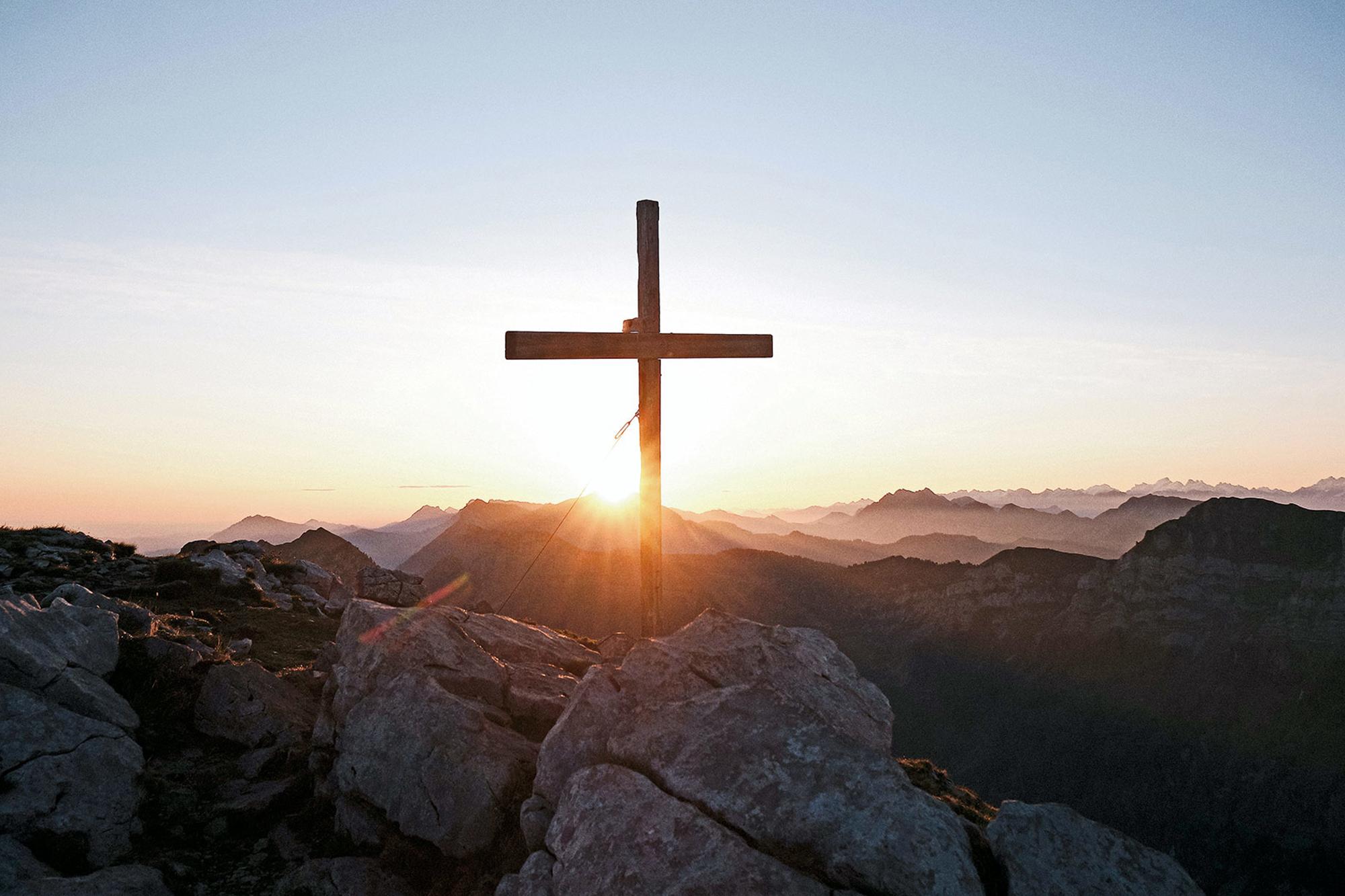 Ett stort kors som står på ett berg - i bakgrunden syns soluppgången och bergstoppar