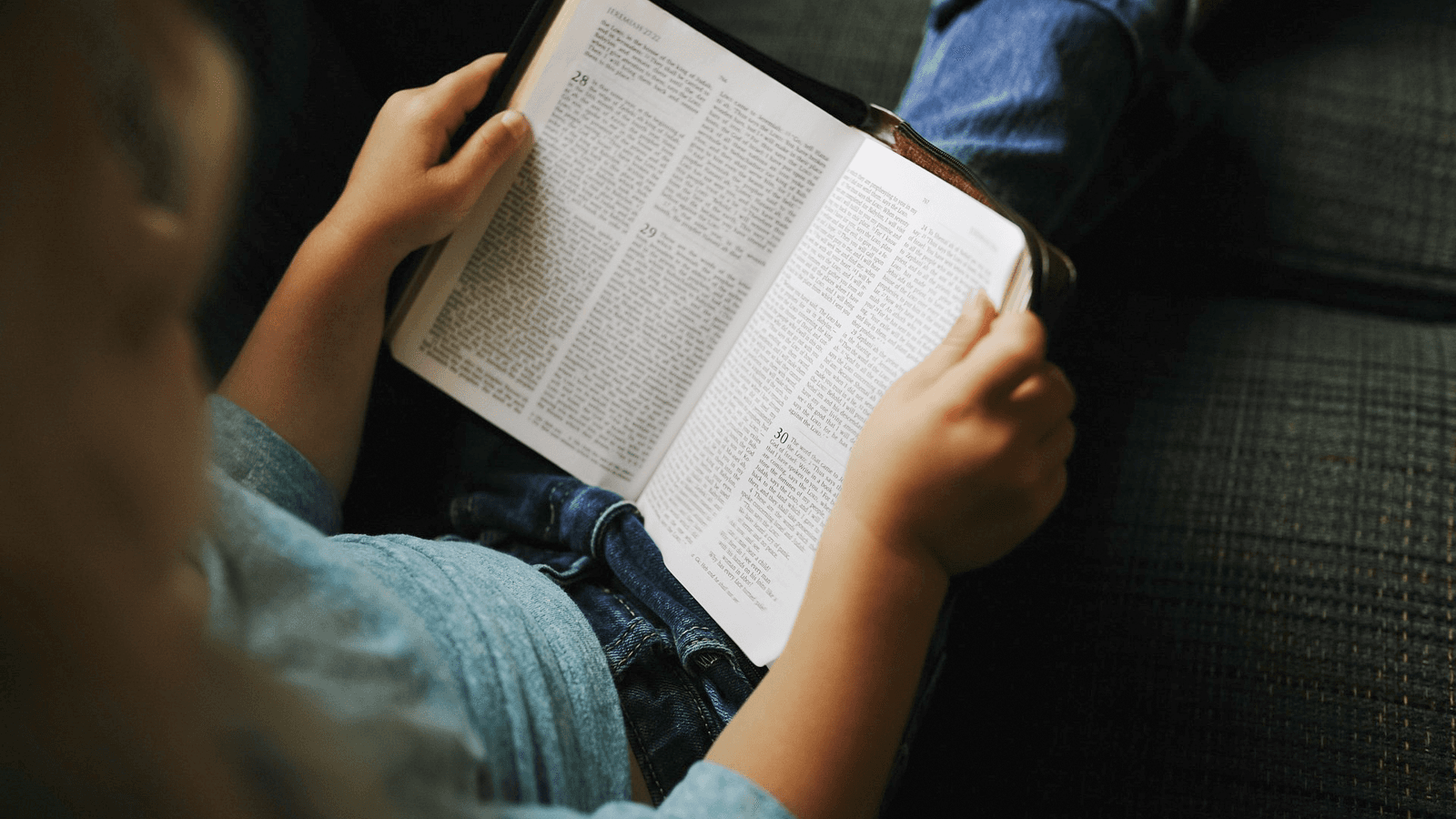 En ung tjej sitter och läser i bibeln, bilden är tagen uppifrån.