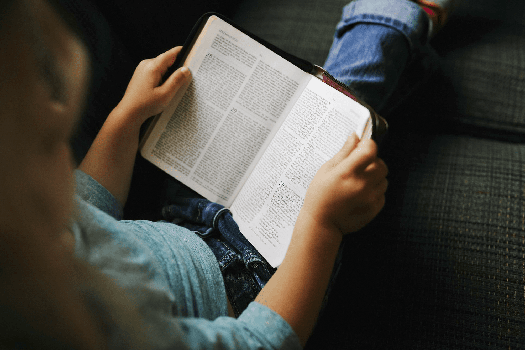 En ung tjej sitter och läser i bibeln, bilden är tagen uppifrån.