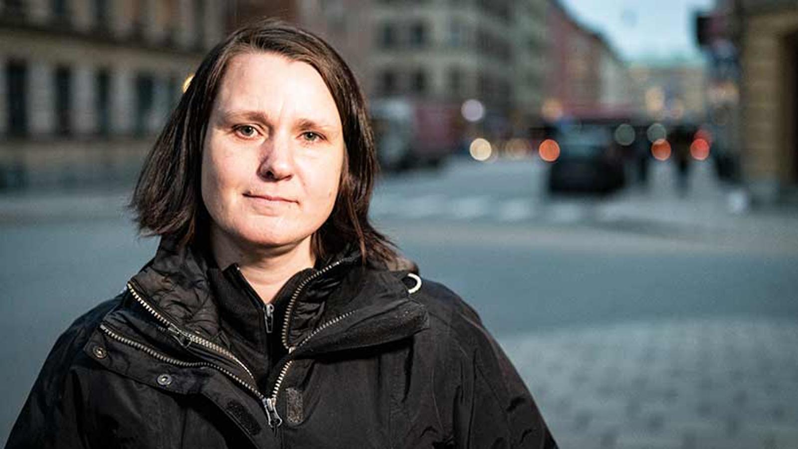 Porträttbild av Kamilla Lindstedt som tittar in i kameran. Hon står utomhus på en gatan, och i bakgrunden syns byggnader.