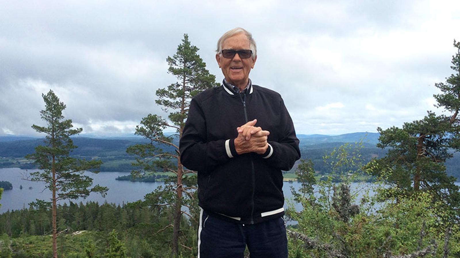 Porträttbild av Bengt Johansson. Han står utomhus med knutna händer och med blicken i kameran. Bakom honom syns skog och en sjö.