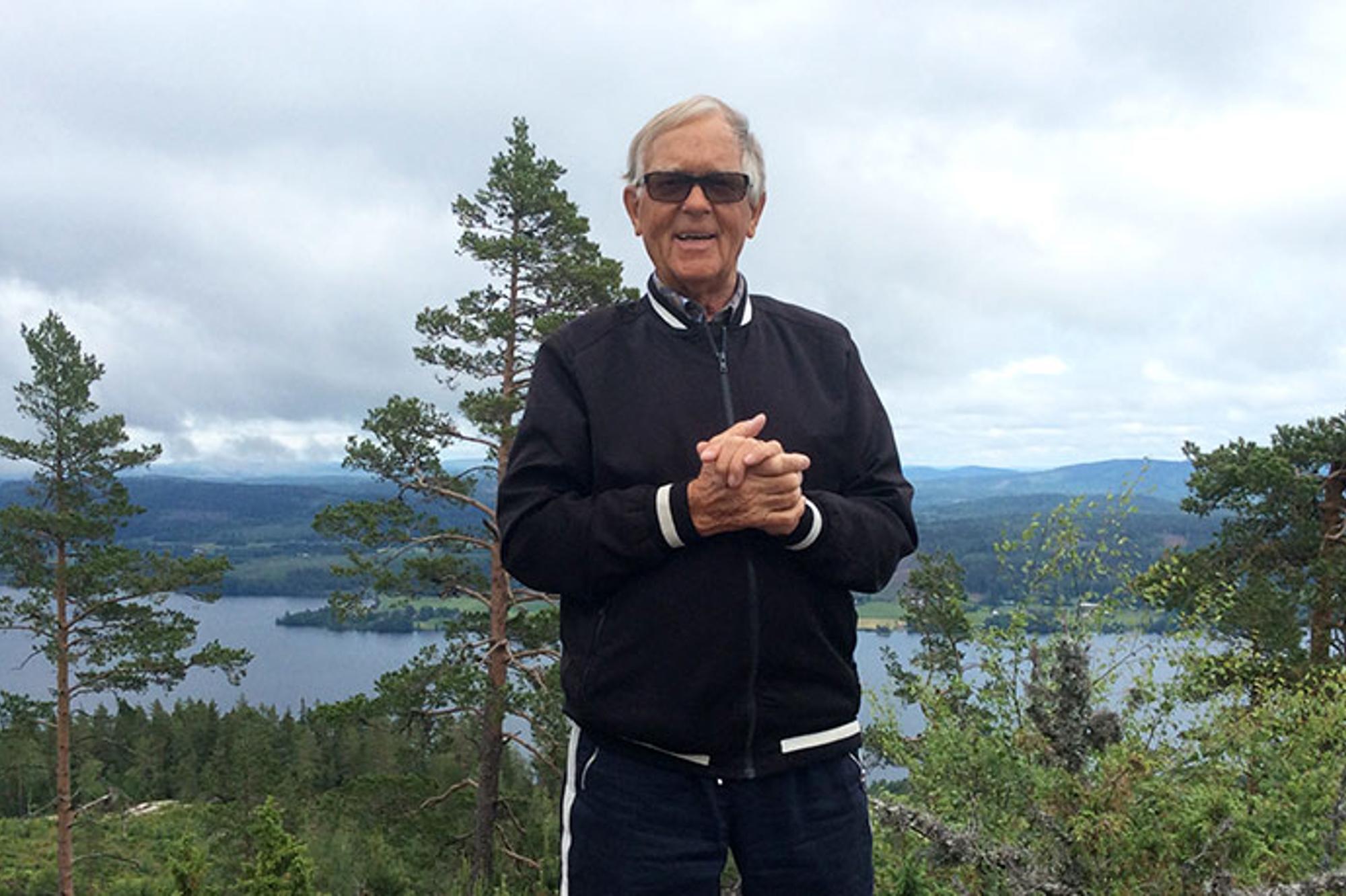 Porträttbild av Bengt Johansson. Han står utomhus med knutna händer och med blicken i kameran. Bakom honom syns skog och en sjö.