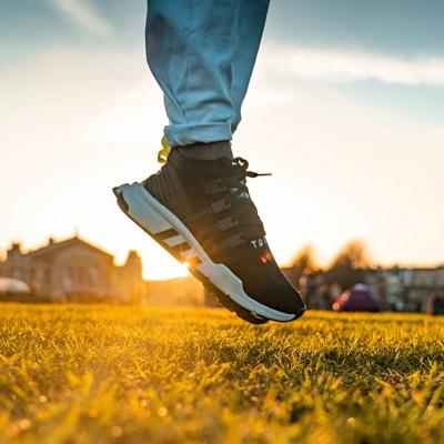Närbild på ett par ben med sneakers på fötterna som hoppar ovanför en gräsmatta med hus och människor i bakgrunden.