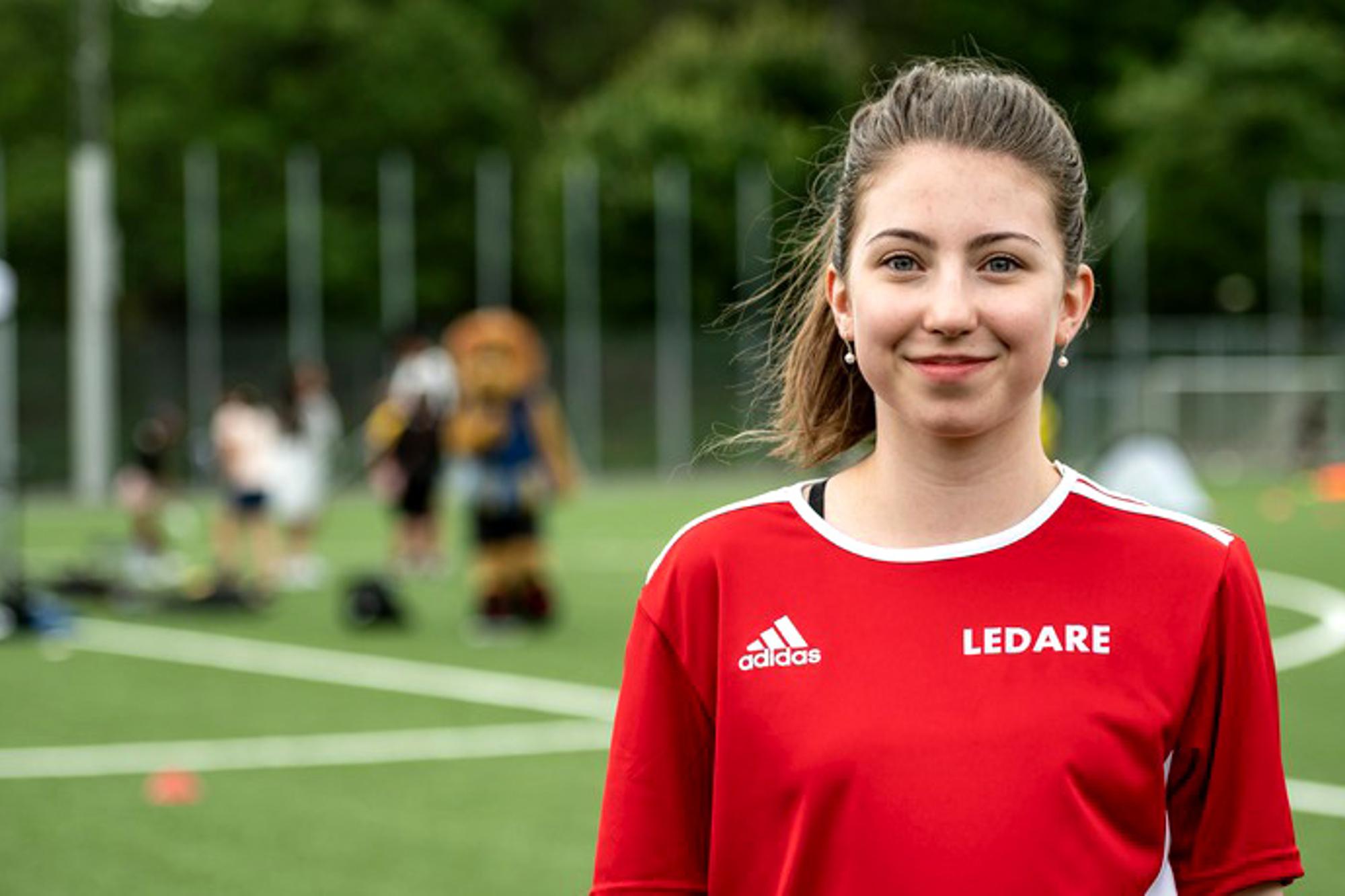 En bild på Julia Kaslin som är ny som ledare. Hon står på en fotbollsplan och bär en tröja med texten "Ledare" på.