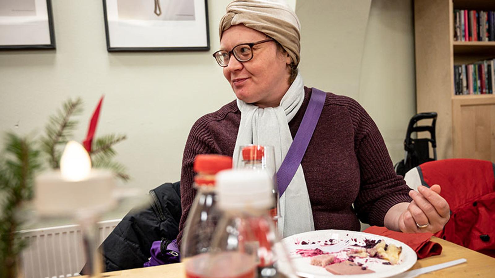 En kvinna, Olena, som sitter vid ett bord på Frälsningsarméns sociala center. Hon ler och tittar åt vänster om kameran. På bordet står en flaska julmust och en tallrik med julmat.