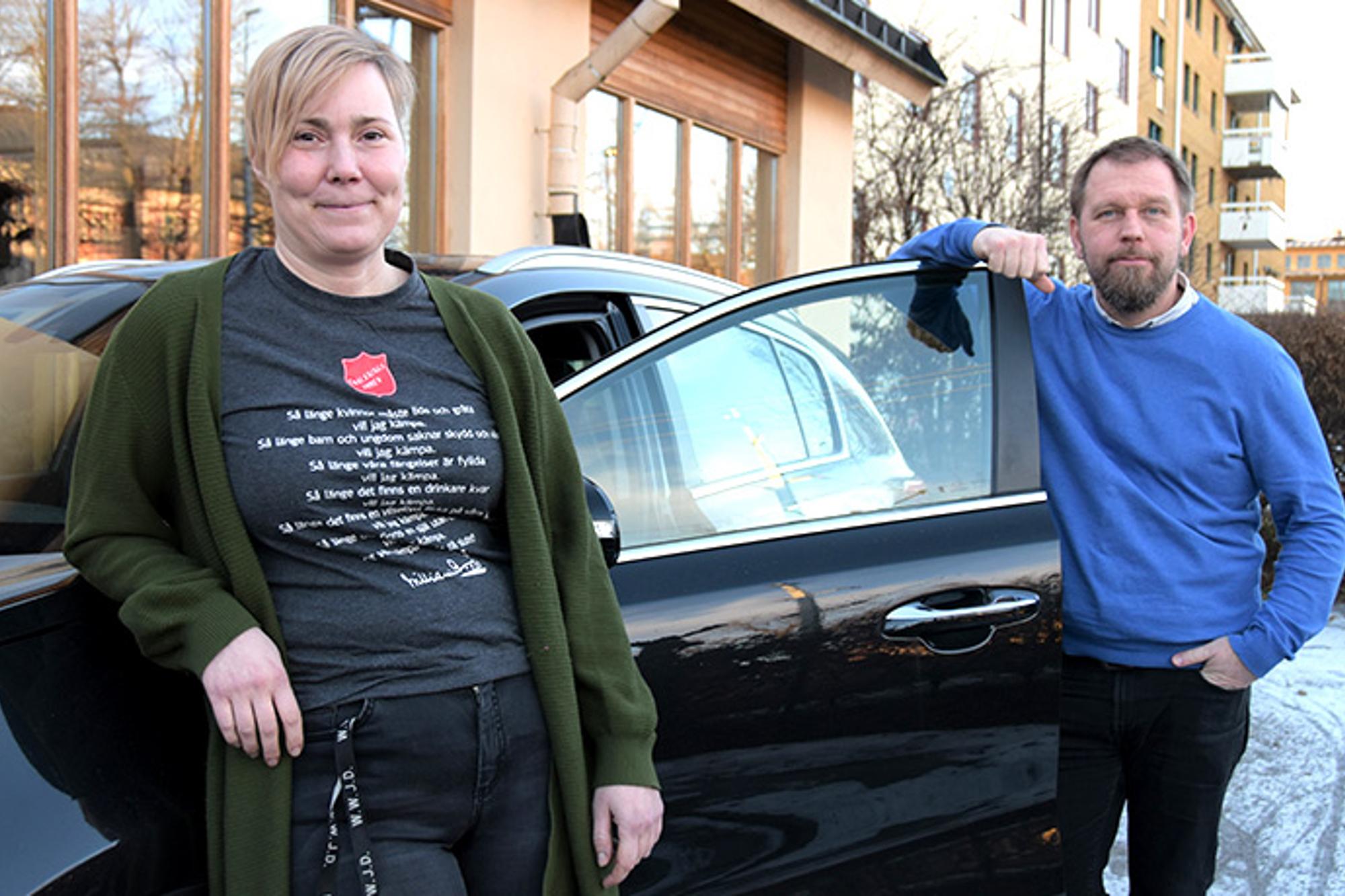 Ulrika och Jorma som arbetar på Brobygget, Frälsningsarmén. De står lutade mot en bil och tittar in i kameran.