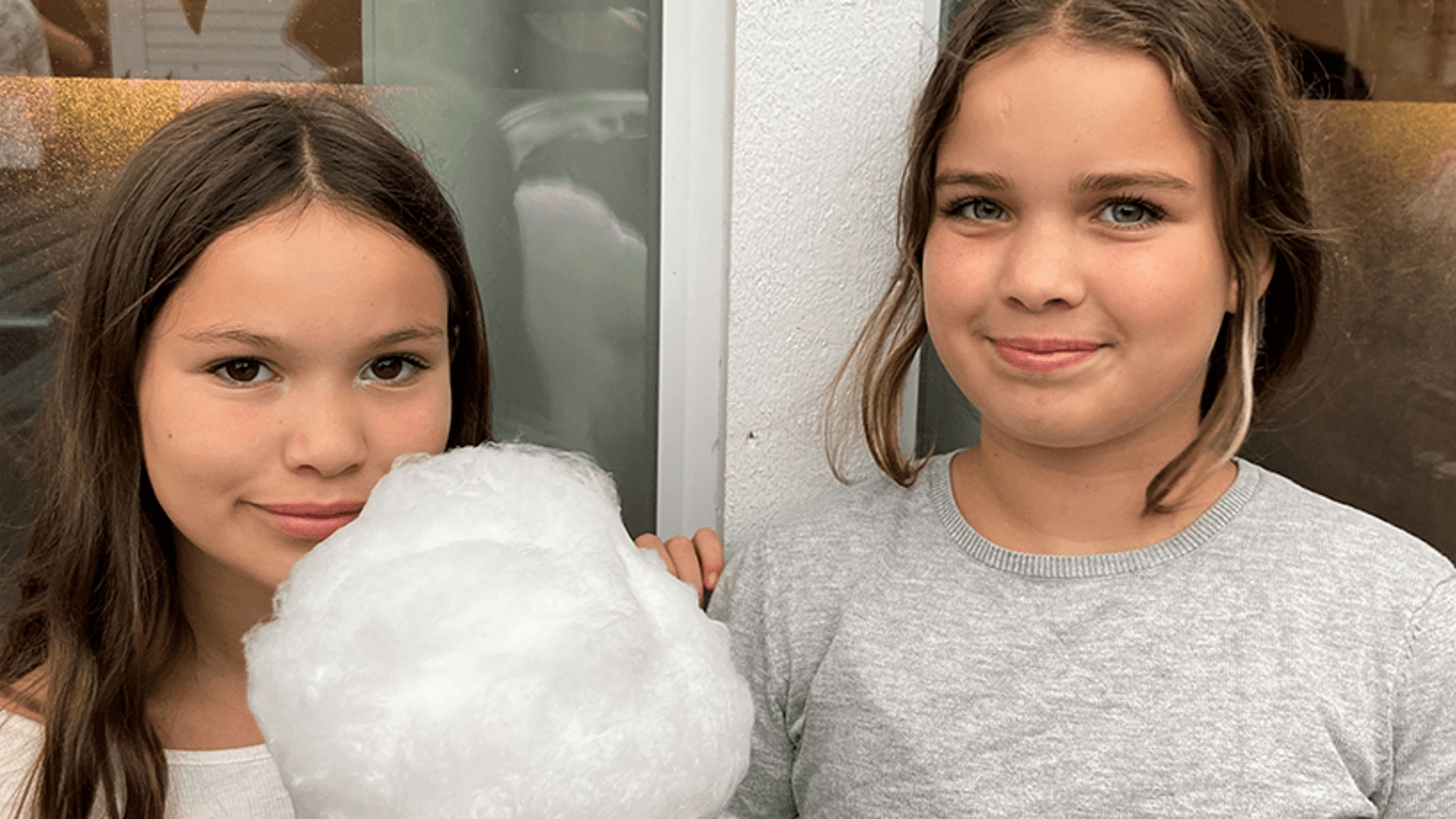 Två unga flickor som tittar in i kameran och håller i sockervadd.