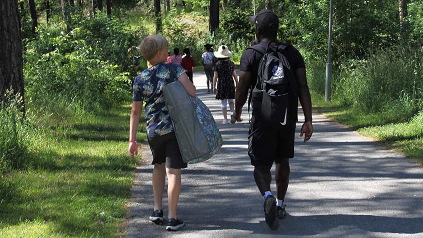 Ett gäng barn och aktivitetsledare som går på en väg i naturen.
