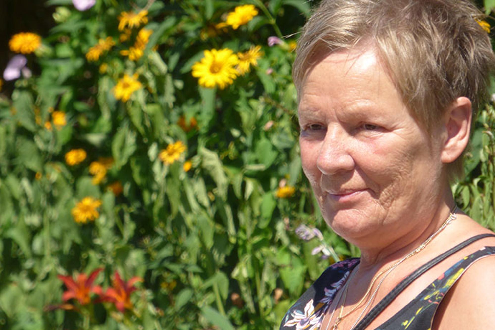 Porträttbild av Ankie Dahlstedt. Hon tittar till vänster om kameran, och i bakgrunden syns blommor.