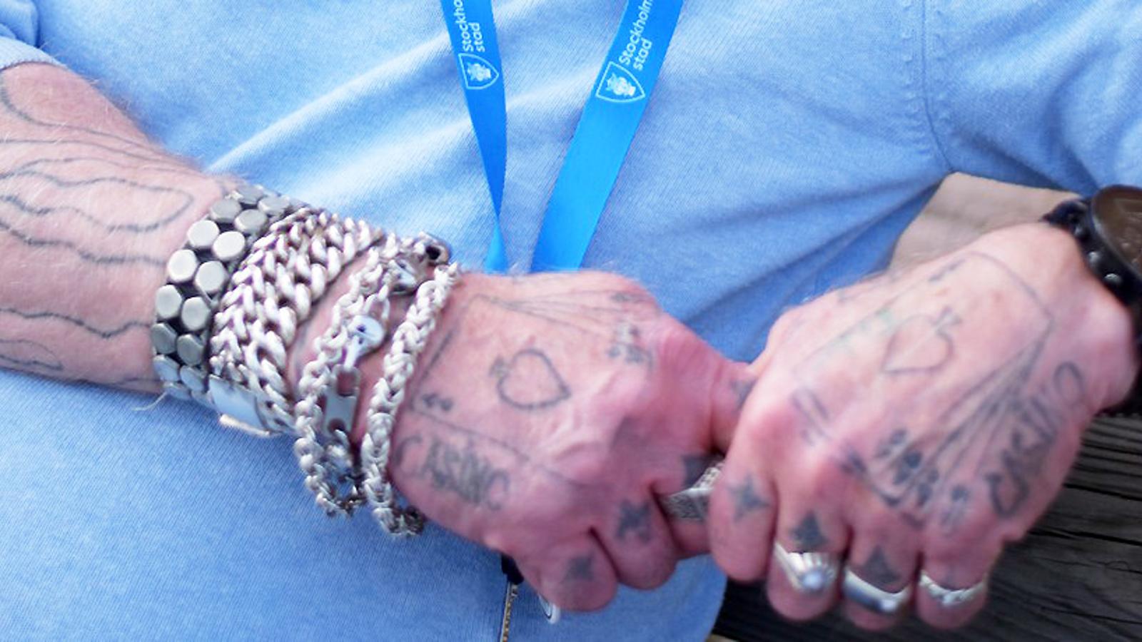 Lars händer som är fulla av tatueringar, fingrarna är prydda av kraftiga silverringar och på ena armleden trängs kedjor.