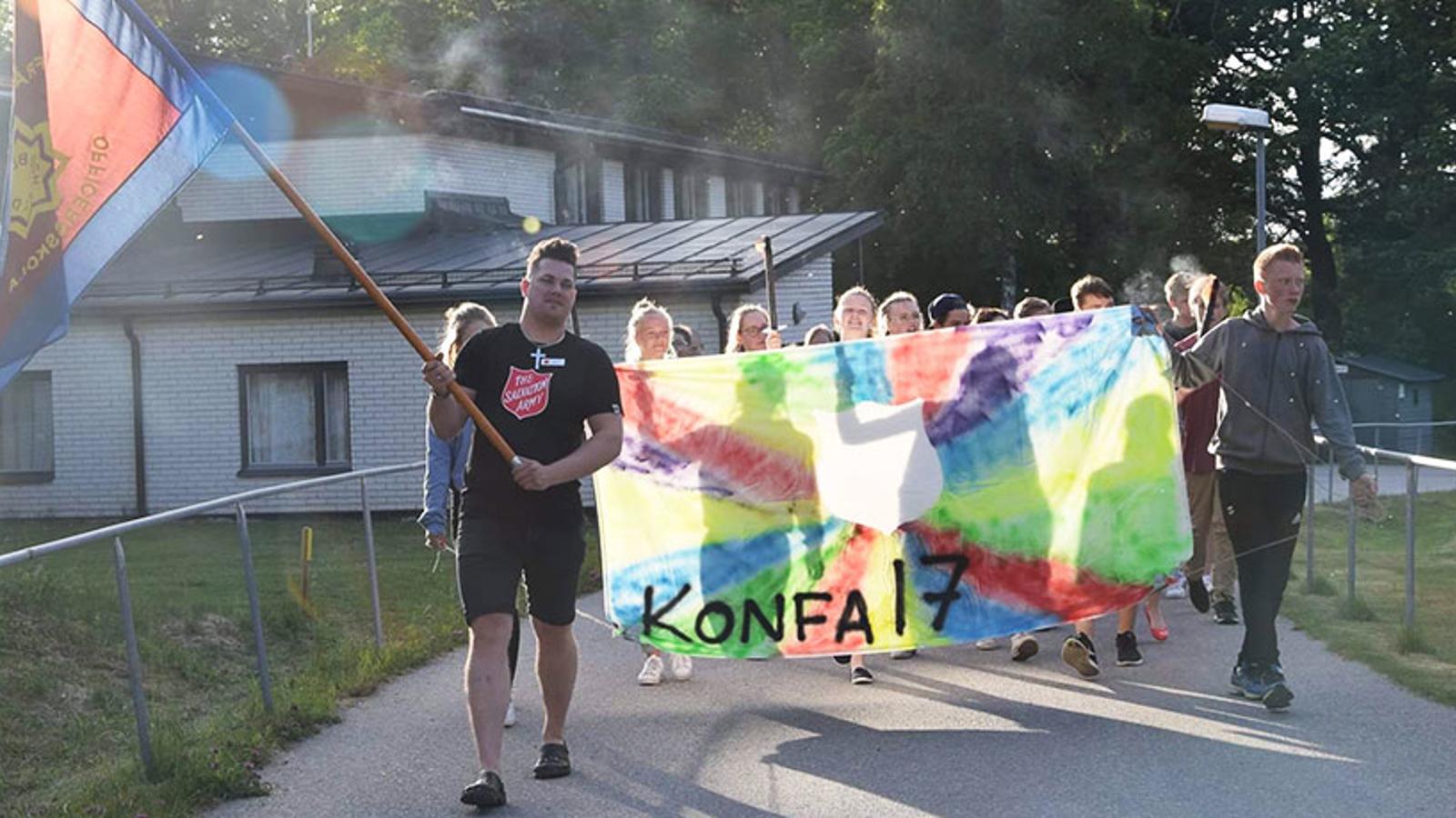 Längst fram går det en man från Frälsningsarmén som håller i en flagga. Bakom honom går ett gäng konfirmander som håller i ett färgglatt skynke med texten "Konfa 17".