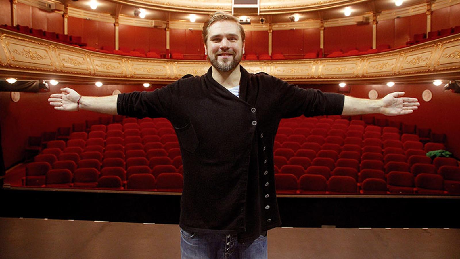 Bild på Linus Fagerström som står i en teater och ler mot kameran. Han håller båda armarna utsträckta i luften.
