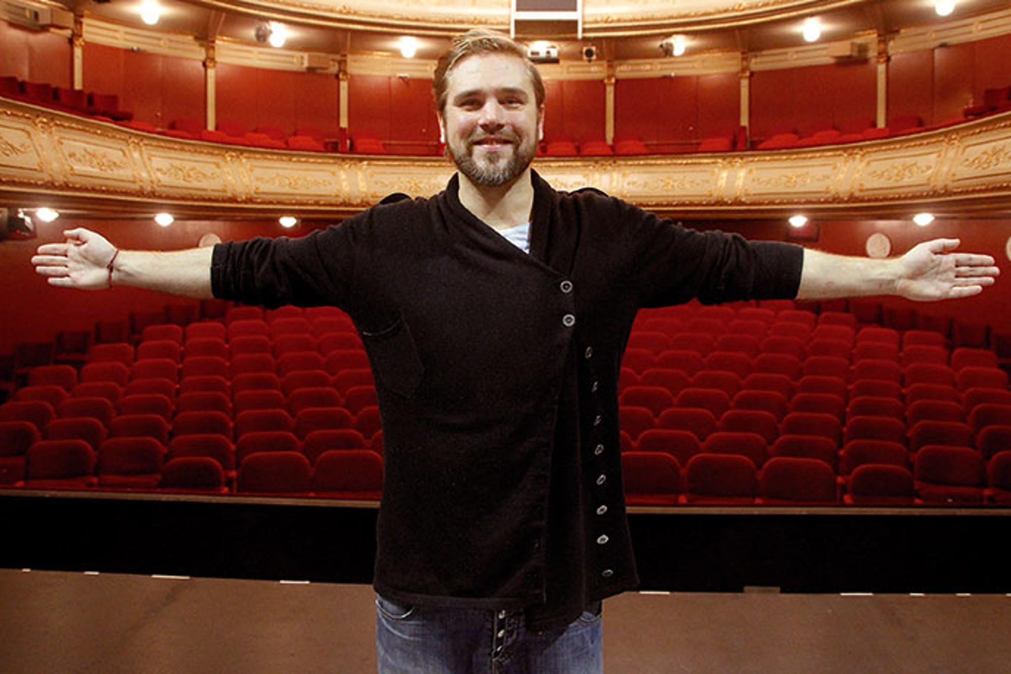 Bild på Linus Fagerström som står i en teater och ler mot kameran. Han håller båda armarna utsträckta i luften.