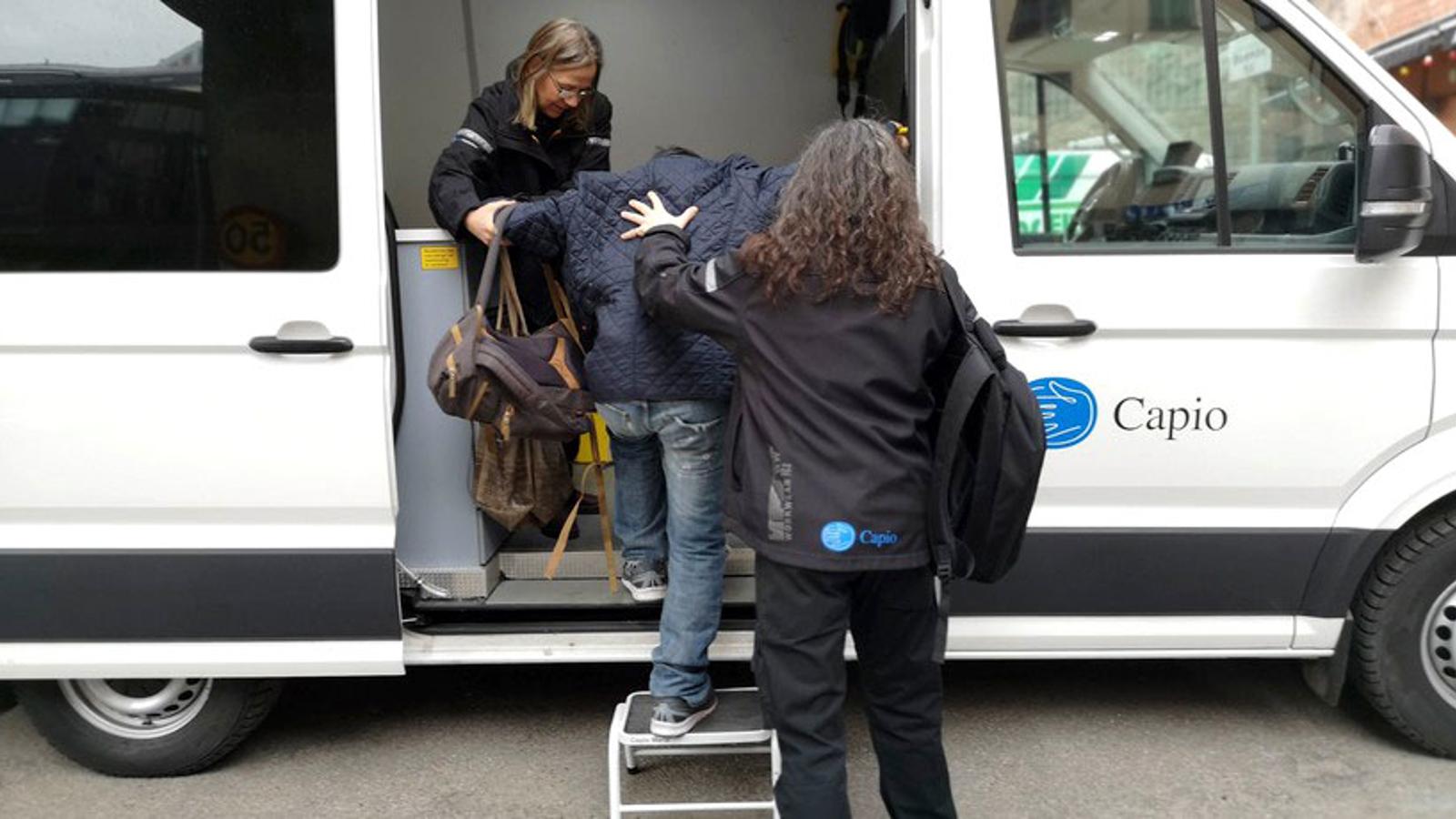 Två kvinnor som hjälper en man in i en av Pelarbacken vårdcentrals bussar.