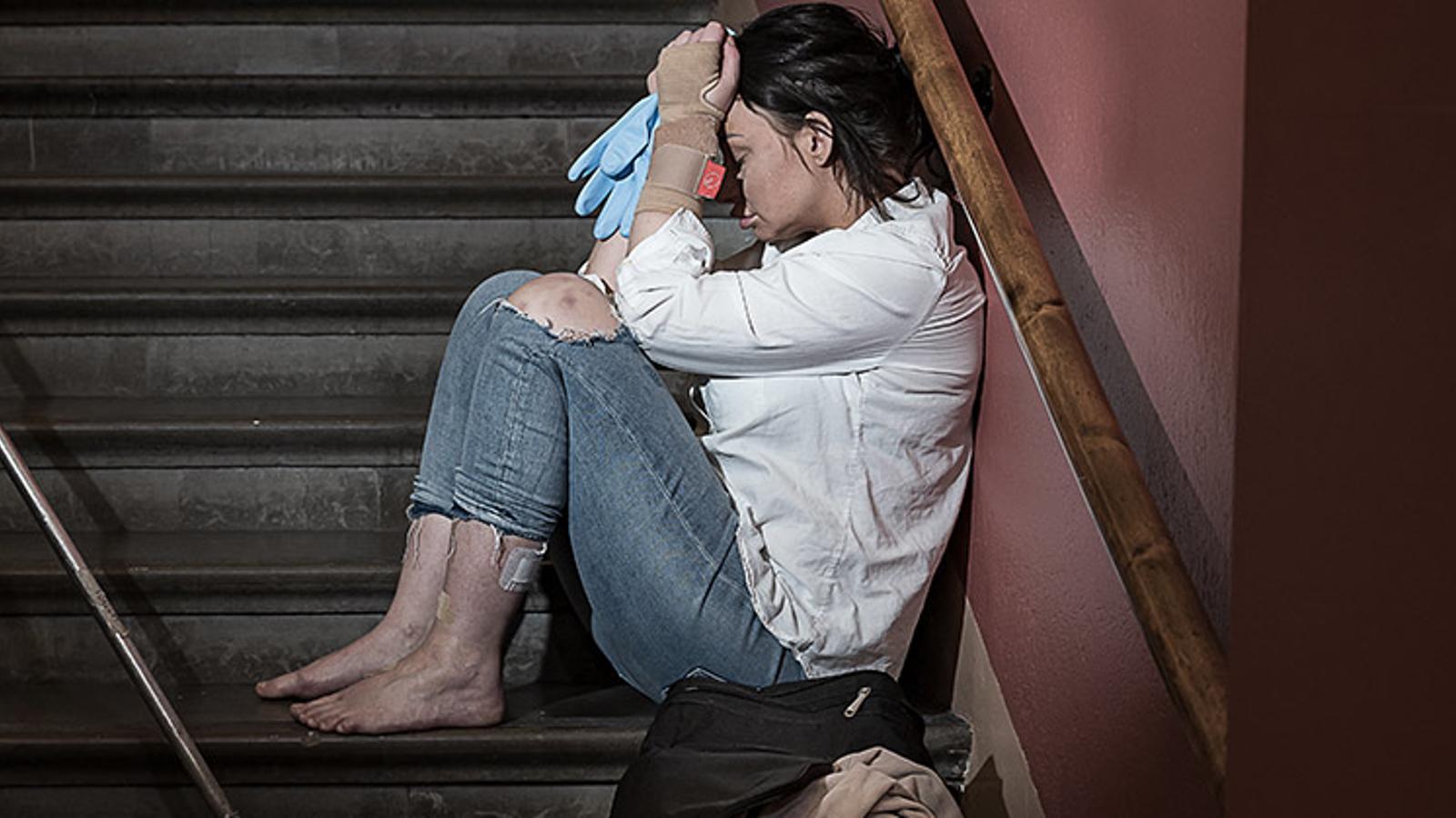 En ung kvinna sitter i en trapp med bara fötter och håller händerna för ansiktet.