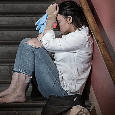 En ung kvinna sitter i en trapp med bara fötter och håller händerna för ansiktet.