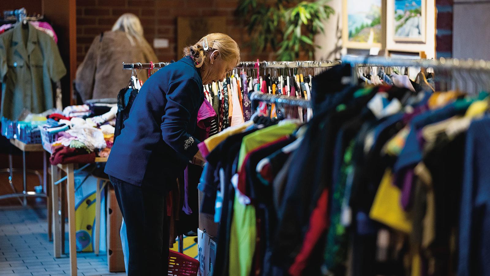 Alice Jönsson, som ansvarar för loppisen, håller ordning bland varorna. Hon står vid några klädhängare och sorterar kläder.