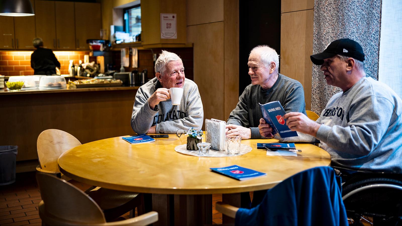 Bengt Lundén, Kent Schlyter och Lasse Ohlsson som sitter runt ett bord och fikar på kafé Oasen. I bakgrunden syns ryggtavlan på en person som står i ett kök.