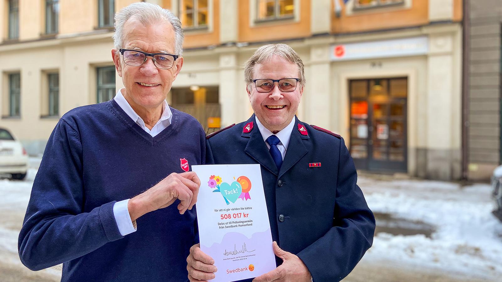 Lars Beijer och Per-Uno Åslund står utanför Frälsningsarméns högkvarter och håller i diplomet från Swedbank Robur Humanfond.