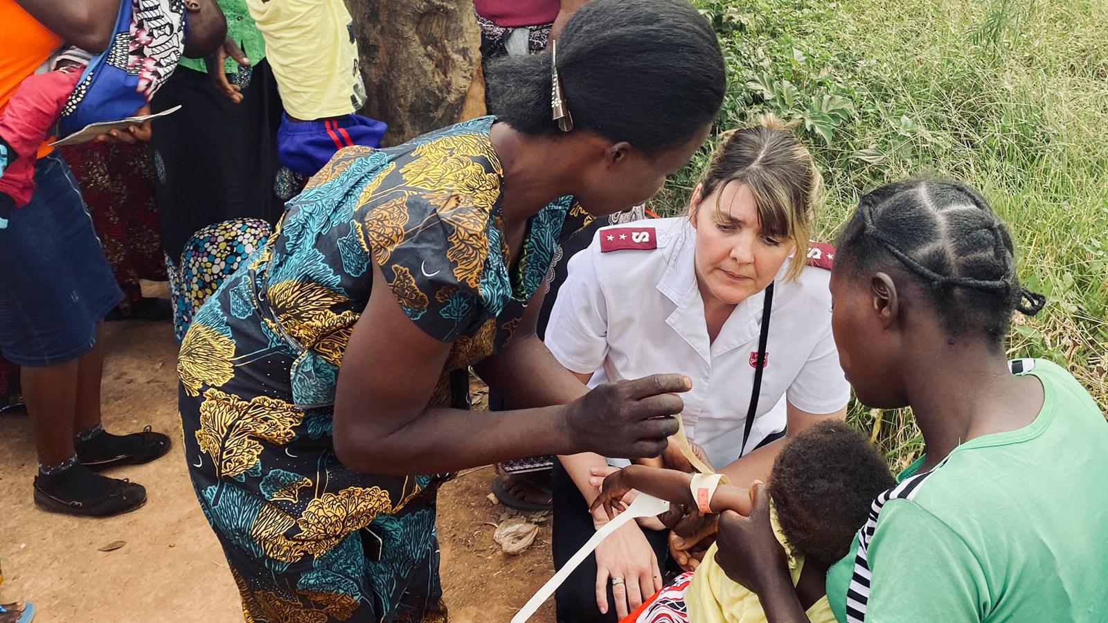 En kvinna med Frälsningsarméns uniform samtalar med några kvinnor och ett barn utom hus i Zambia. I bakgrunden syns fler personer