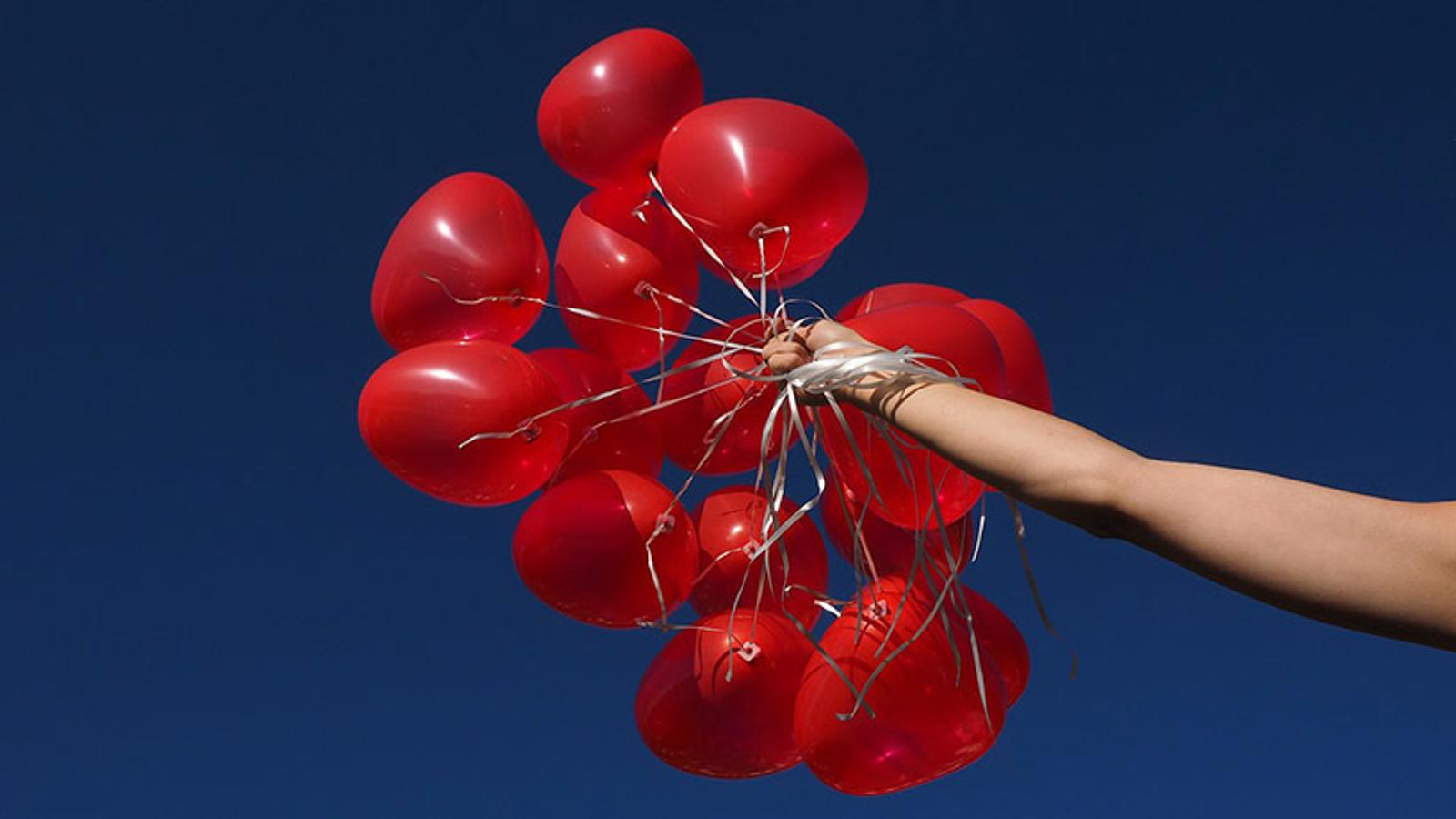En arm som håller i ett gäng röda ballonger.