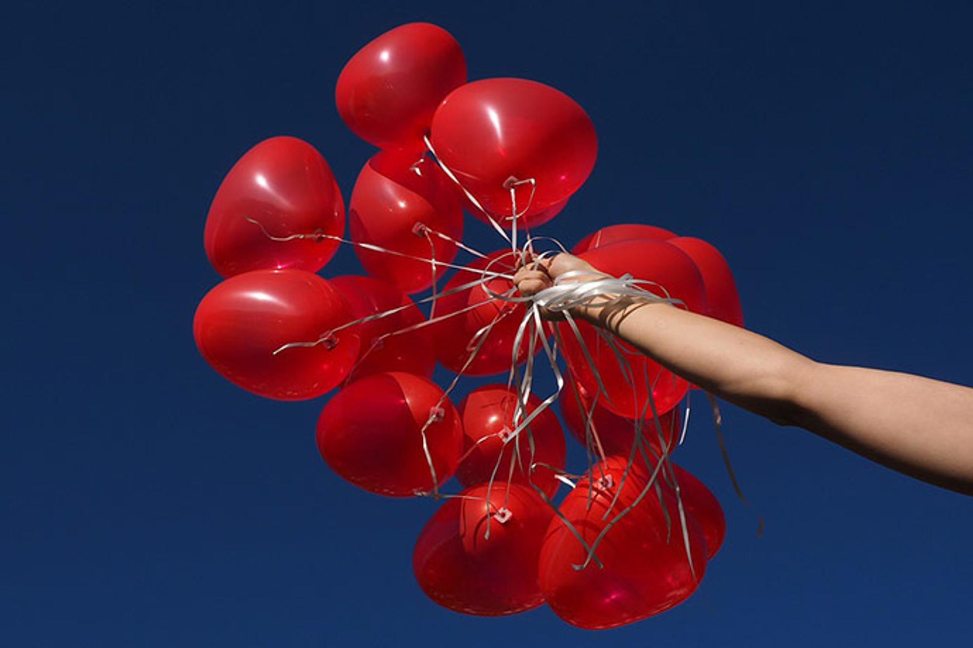 En arm som håller i ett gäng röda ballonger.