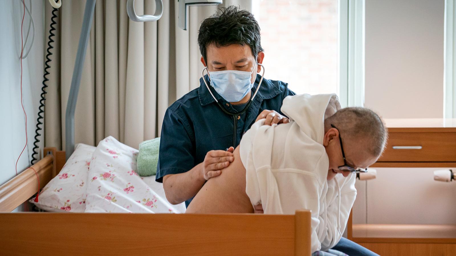 En sjuksköterska lyssnar på en äldre mans andning genom ett stetoskop.